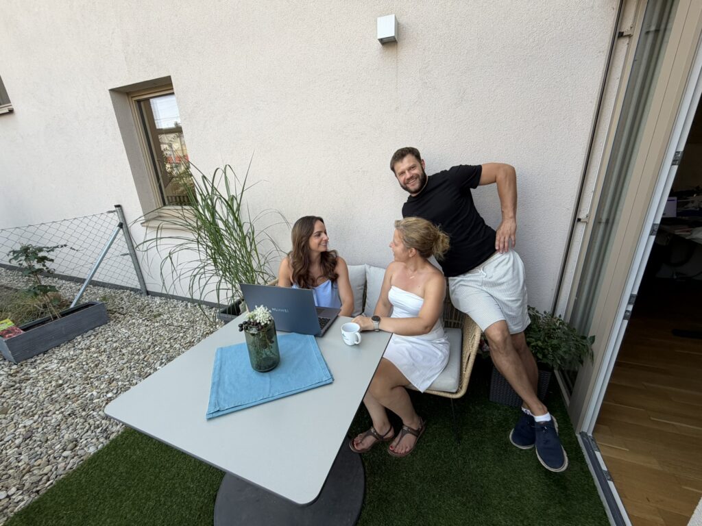 3 Leute auf einer Couch im Freien und ein Tisch mit einem Laptop drauf.